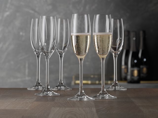 Six SPIEGELAU Festival Champagne flutes on a table. In the foreground two of those glasses are filled with sparkling wine.<br/>