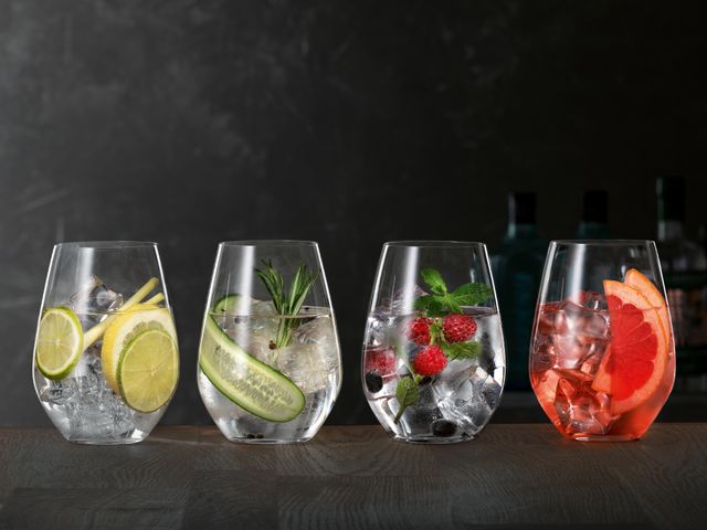 SPIEGELAU Gin und Tonic Gläser auf einem hölzernen Sideboard, jedes davon gefüllt mit einem anderen Gin Cocktail.<br/>