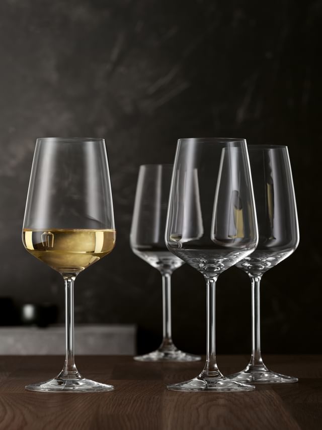 Vier Weißweingläser von SPIEGELAU Style auf einem Holztisch. Ein Glas ist mit Weißwein gefüllt.<br/>