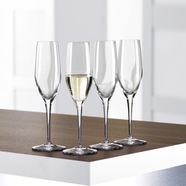 Four SPIEGELAU Authentis Champagne flutes on a table, one of them is filled with sparkling wine.<br/>