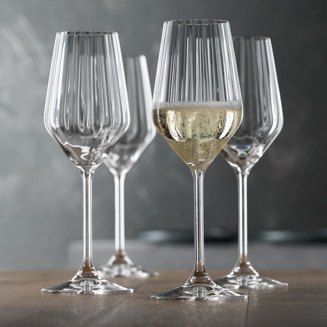 Four SPIEGELAU Lifestyle Champagne glasses on a wooden table. One of them is filled with Champagne.<br/>