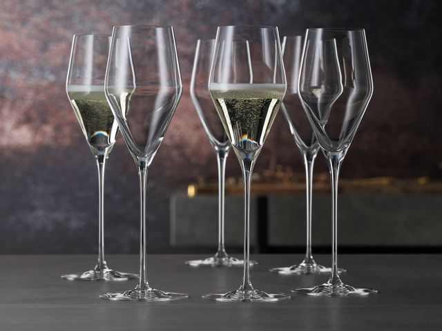 Six SPIEGELAU Definition Champagne glasses of which two are filled with sparkling wine are standing on a table.<br/>