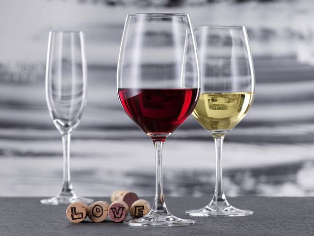 Ein mit Rotwein gefülltes Bordeauxglas und ein mit Weißwein gefülltes Weißweinglas aus der SPIEGELAU Winelovers Kollektion. Im Hintergrund ist eine leere Champagnerflöte zu sehen. Hinter dem Bordeauxglas liegen fünf Korken, vier davon zeigen Buchstaben des Wortes LOVE.<br/>