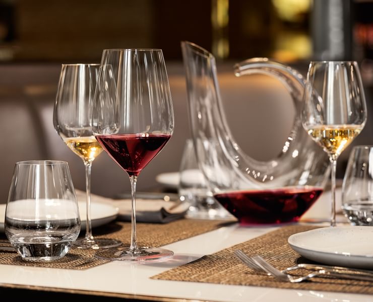 A laid dinner table with hand made SPIEGELAU Highline glasses. The red wine glass is filled with red wine and the white wine glass is filled with white wine. The SPIEGELAU Authentis Casual tumbler besides them is filled with water. In the background there is a hand made Highline decanter and more filled glasses.<br/>